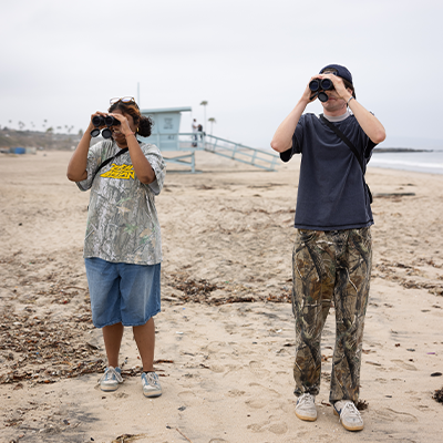 environmental science students looking through binoculars on beach